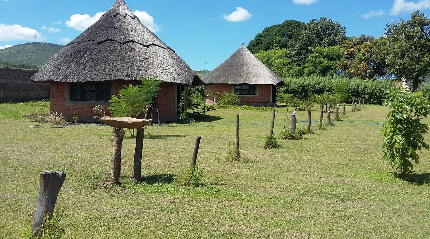 Two thatched chalets on the lawn, with the Chipata hills behind